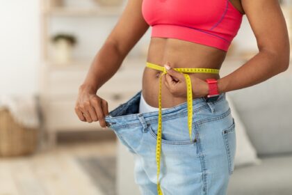 Woman After Weight-Loss Measuring Waist Wearing Oversize Jeans Indoors, Cropped